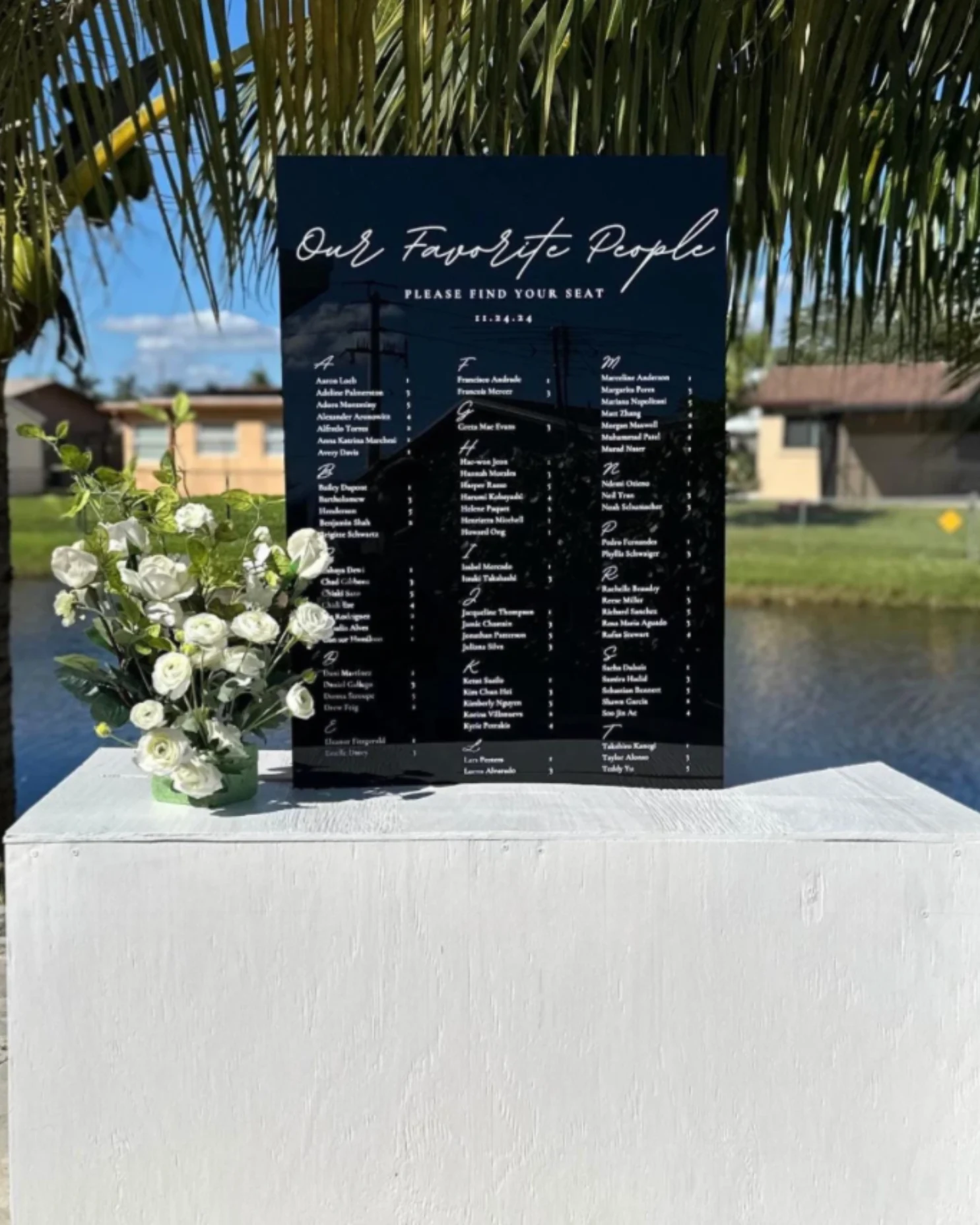Black seating chart with white lettering and a white floral accent.